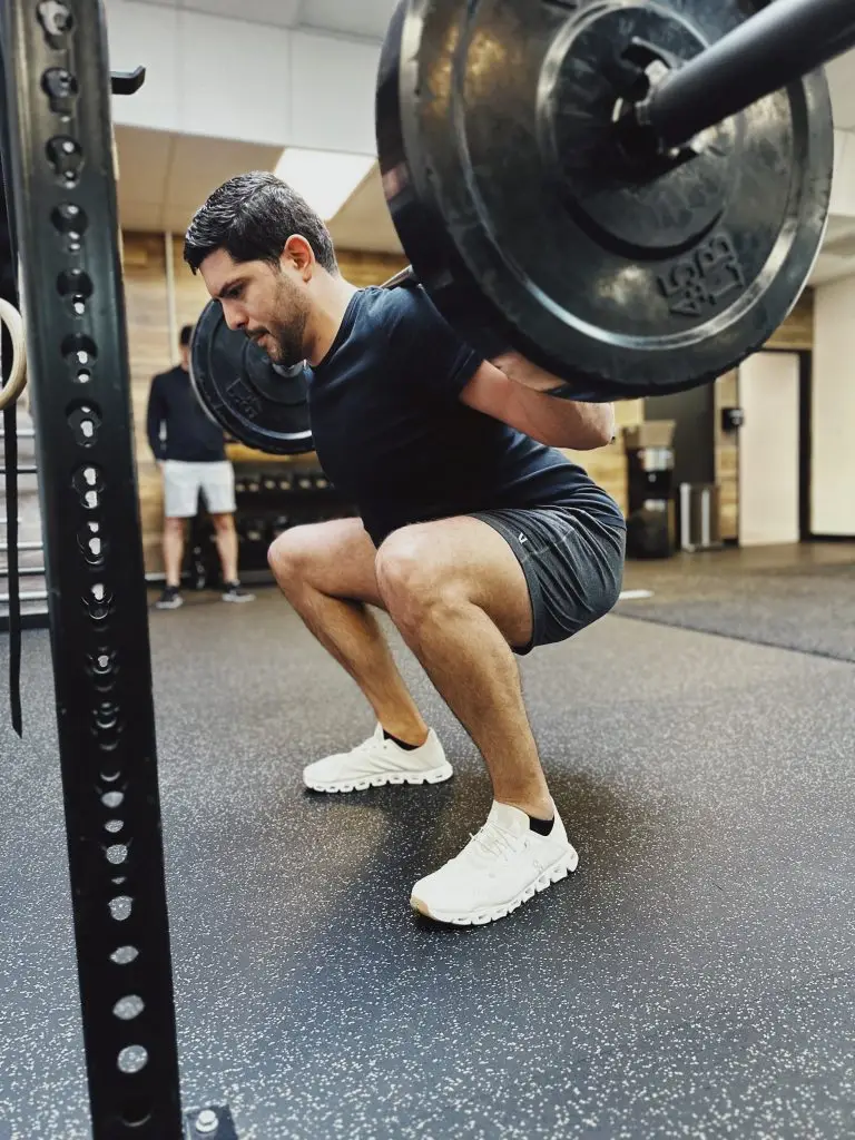 Man wearing a dark shirt and shorts performing a barbell back squat