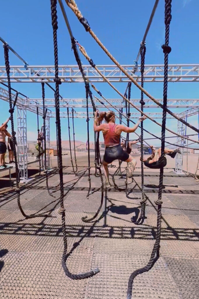 Female in her thirties completing a rope obstacle at a Tough Mudder race
